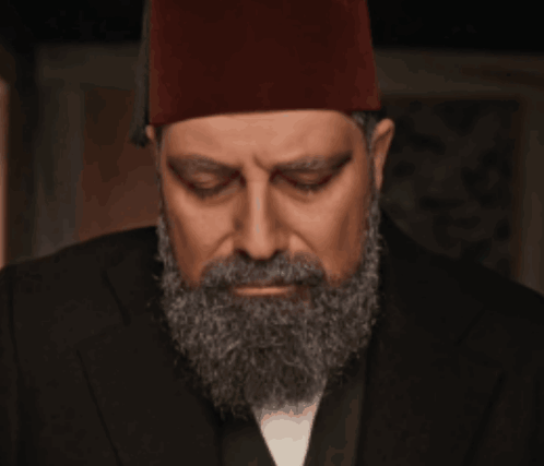 A Man With A Beard And A Red Hat Looks Down GIF