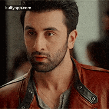A Man With A Beard And A Red Leather Jacket Is Looking At The Camera . GIF