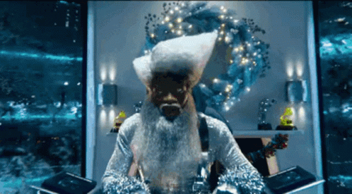 A Man With A Beard And A Santa Hat Is Sitting In Front Of A Wreath GIF