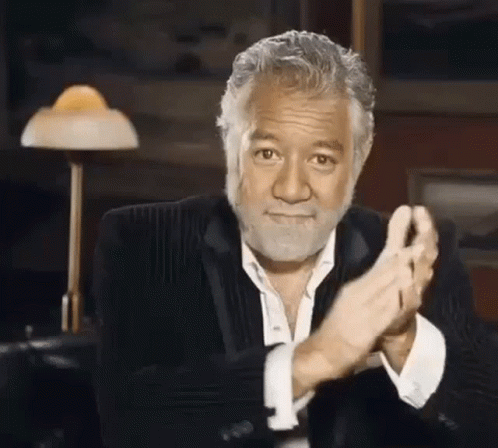 A Man With A Beard And A Suit Is Clapping His Hands In A Room . GIF