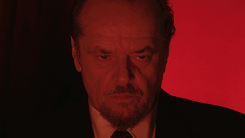 A Man With A Beard And A Suit Is Looking At The Camera With A Red Background GIF