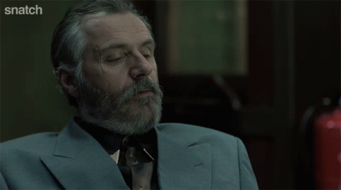 A Man With A Beard And A Suit Is Sitting In Front Of A Screen That Says Snatch GIF
