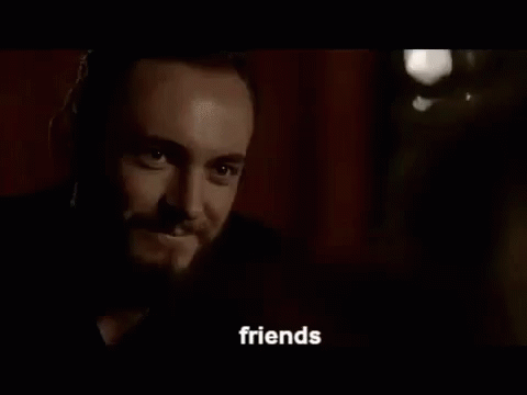 a man with a beard and a tattoo on his face is talking to someone in a dark room .