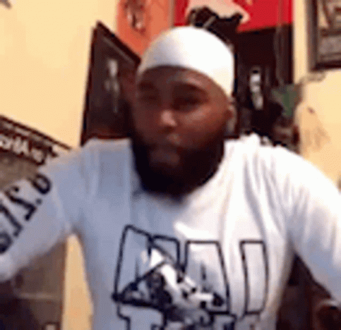 A Man With A Beard And A White Headband Is Wearing A White Shirt . GIF