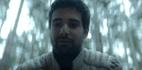 A Man With A Beard And A White Jacket Looks At The Camera GIF