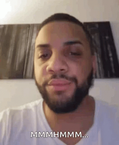 A Man With A Beard And A White Shirt Is Making A Funny Face And Saying Mmmmhmm . GIF