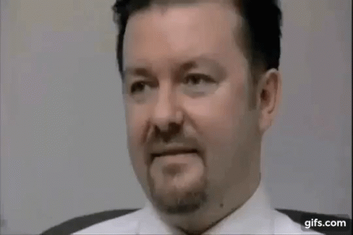 A Man With A Beard And A White Shirt Is Sitting In A Chair . GIF