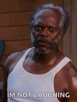A Man With A Beard And A White Tank Top Is Laughing . GIF