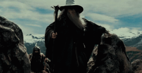 A Man With A Beard And A Wizard Hat Is Walking Through A Rocky Area GIF