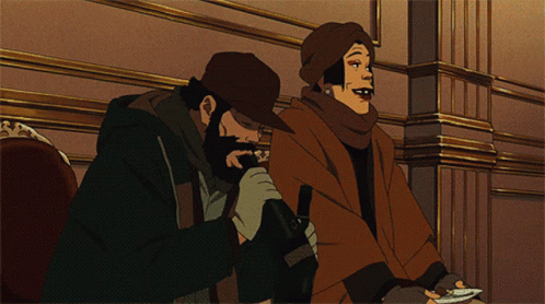 A Man With A Beard And A Woman With A Scarf Around Their Neck Are Sitting Next To Each Other GIF