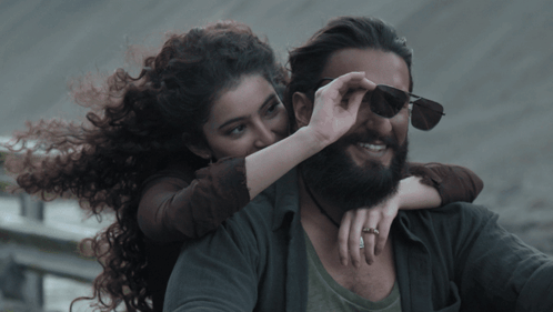 A Man With A Beard And A Woman With Curly Hair On His Back GIF