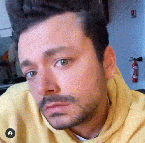 A Man With A Beard And A Yellow Hoodie Is Making A Face . GIF