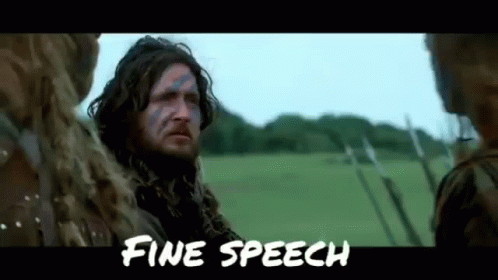 A Man With A Beard And Blue Paint On His Face Is Standing In A Field With Other People . GIF