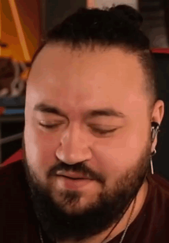 A Man With A Beard And Bun Is Wearing Headphones And Making A Face . GIF