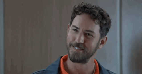 A Man With A Beard And Curly Hair Is Smiling While Wearing An Orange Shirt . GIF