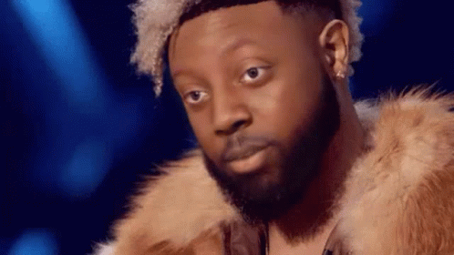 A Man With A Beard And Curly Hair Is Wearing A Fur Coat . GIF
