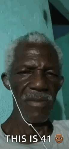 A Man With A Beard And Ear Buds Is Wearing Headphones . GIF