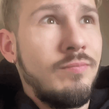 A Man With A Beard And Earrings Is Looking Up At The Camera . GIF