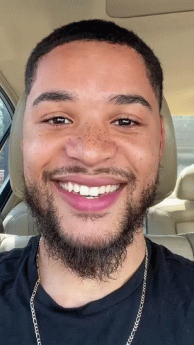 A Man With A Beard And Freckles Is Smiling In The Back Seat Of A Car GIF