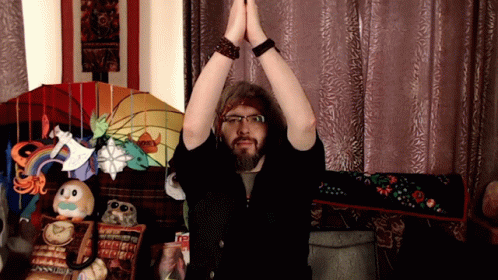 A Man With A Beard And Glasses Holds His Hands Together In Front Of A Stained Glass Lamp That Says Honey GIF