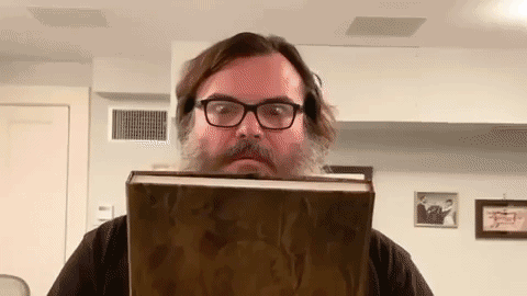 A Man With A Beard And Glasses Is Holding A Large Book In Front Of His Face . GIF