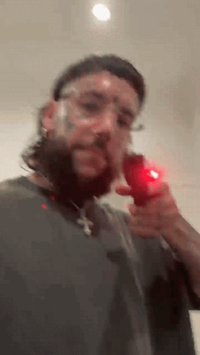 A Man With A Beard And Glasses Is Holding A Red Object In His Right Hand . GIF
