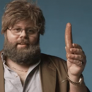 A Man With A Beard And Glasses Is Holding A Sausage In His Hand GIF