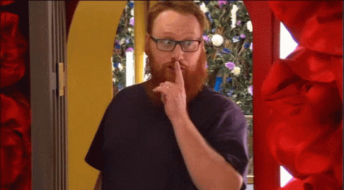 A Man With A Beard And Glasses Is Holding His Finger To His Lips GIF