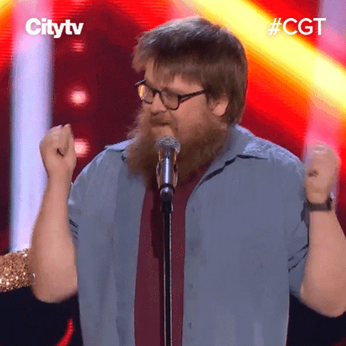 A Man With A Beard And Glasses Is Singing Into A Microphone With The Hashtag #Cgt Behind Him GIF