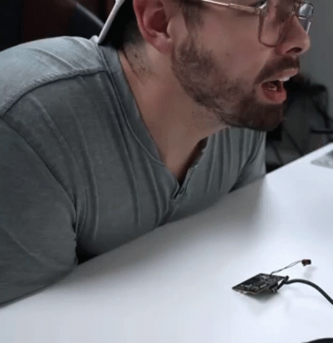 Bearded Man With Glasses Sitting At Table With Device GIF