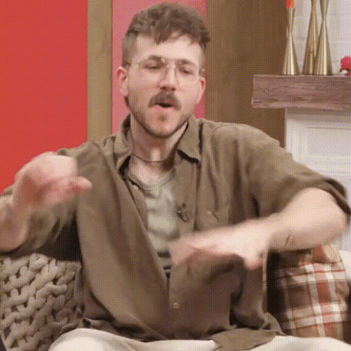 a man with a beard and glasses is sitting on a couch and making a funny face .