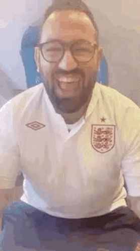 A Man With A Beard And Glasses Is Smiling And Wearing A White Shirt . GIF