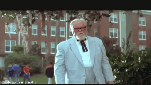 A Man With A Beard And Glasses Is Standing In Front Of A Brick Building . GIF