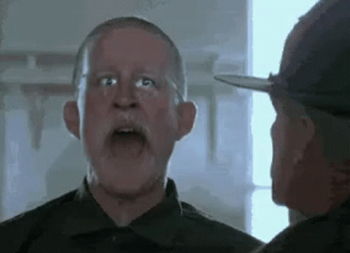 A Man With A Beard And Glasses Is Talking To Another Man In A Military Uniform . GIF