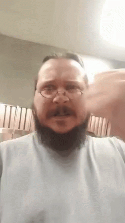 A Man With A Beard And Glasses Is Wearing A White Shirt And Making A Funny Face . GIF