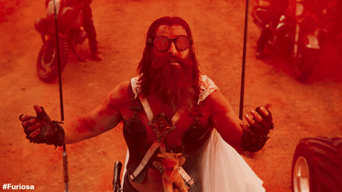 A Man With A Beard And Goggles Holds A Stuffed Animal In His Hand With The Hashtag #Furiosa On The Bottom Right GIF