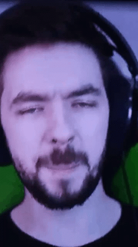 A Man With A Beard And Headphones Is Making A Funny Face . GIF