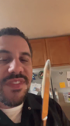 A Man With A Beard And Mustache Is Holding A Knife In Front Of A Refrigerator GIF