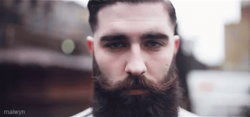 A Man With A Beard And Mustache Is Looking At The Camera With A Serious Look On His Face . GIF