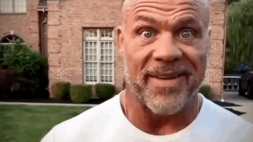 A Man With A Beard And Mustache Is Making A Funny Face In Front Of A Brick House . GIF