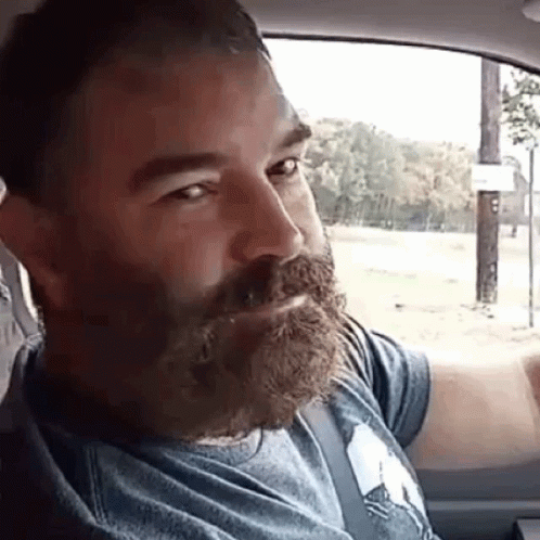 A Man With A Beard And Mustache Is Sitting In A Car . GIF