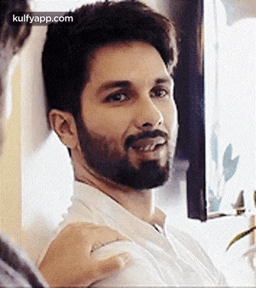 A Man With A Beard And Mustache Is Sitting In Front Of A Window And Smiling . GIF