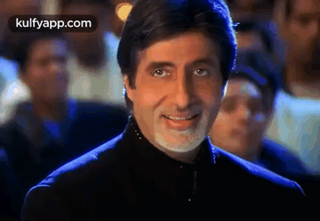 A Man With A Beard And Mustache Is Smiling In Front Of A Crowd . GIF