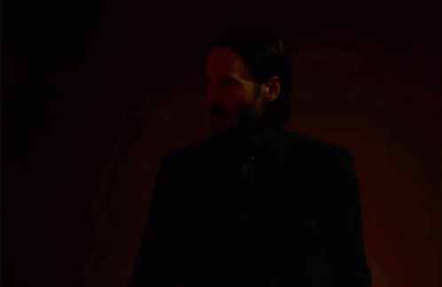 A Man With A Beard And Mustache Is Standing In A Dark Room . GIF
