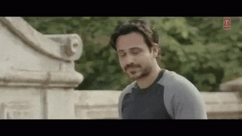 A Man With A Beard And Mustache Is Standing In Front Of A Stone Wall . GIF