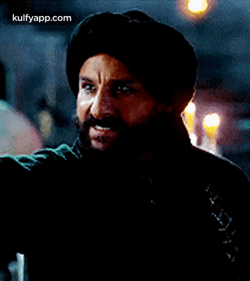 A Man With A Beard And Mustache Is Wearing A Turban And A Black Jacket . GIF