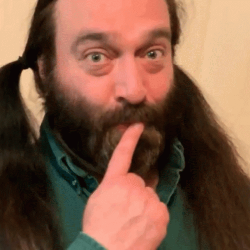 A Man With A Beard And Pigtails Is Holding His Finger To His Lips GIF