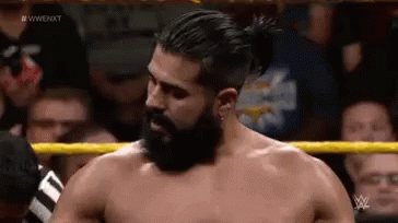 A Man With A Beard And Ponytail Is Standing In A Wrestling Ring . GIF