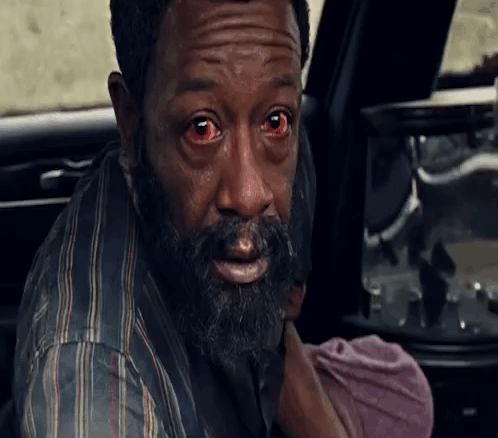 A Man With A Beard And Red Eyes Is Holding A Baby In His Arms . GIF