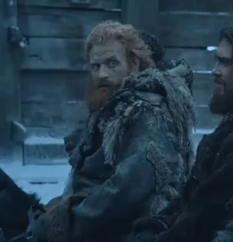 A Man With A Beard And Red Hair Is Sitting Next To Another Man In A Snowy Room . GIF